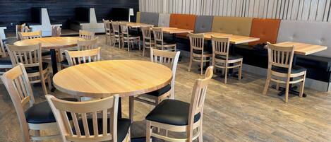 Un comedor moderno con mesas y sillas redondas de madera, una pared de madera oscura y una pared con paneles de madera clara.