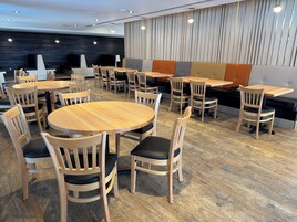 A modern dining area with round wooden tables and chairs, a dark wood wall, and a light wood panel wall.