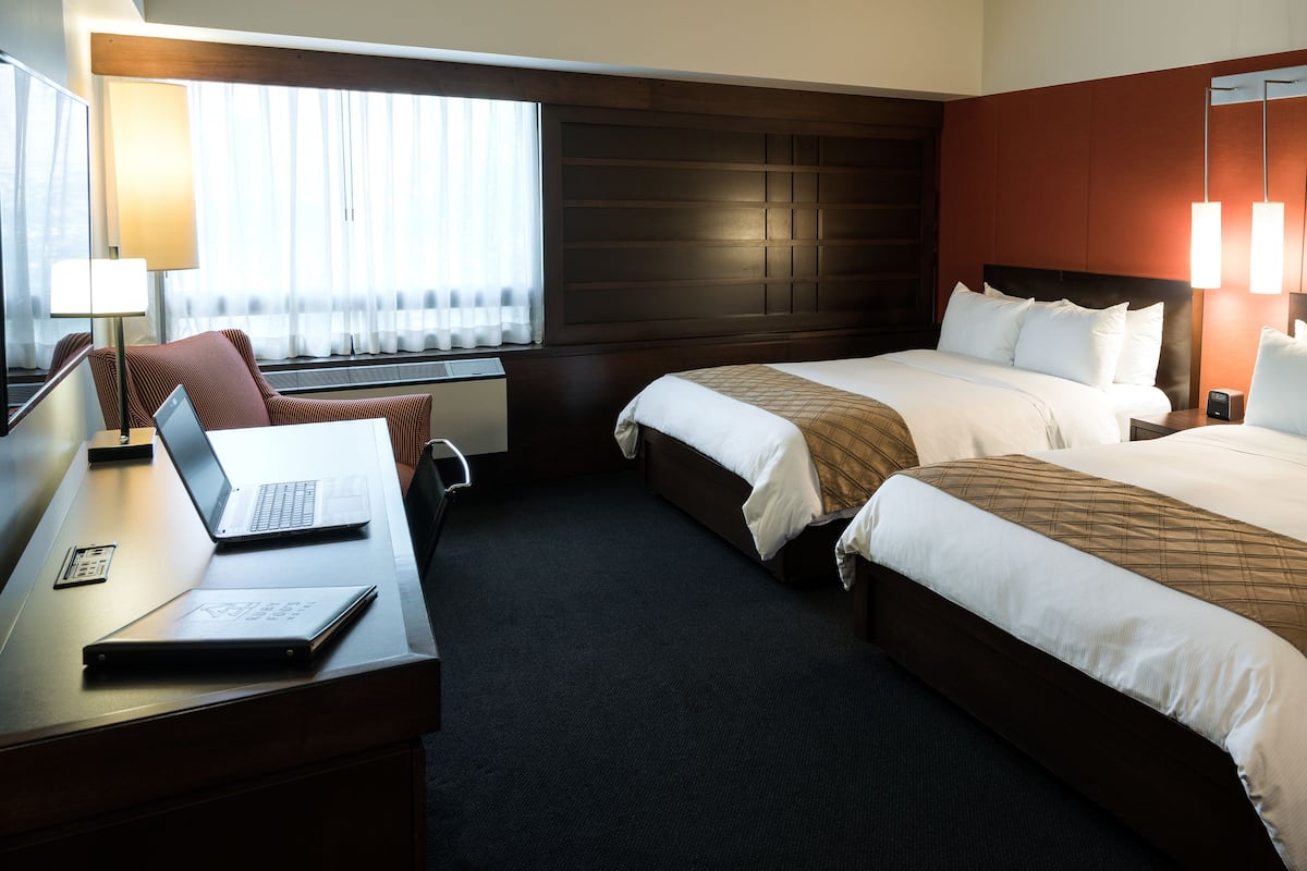 Une chambre d’hôtel avec deux lits, un bureau avec un ordinateur portable, une chaise et une fenêtre avec des rideaux.