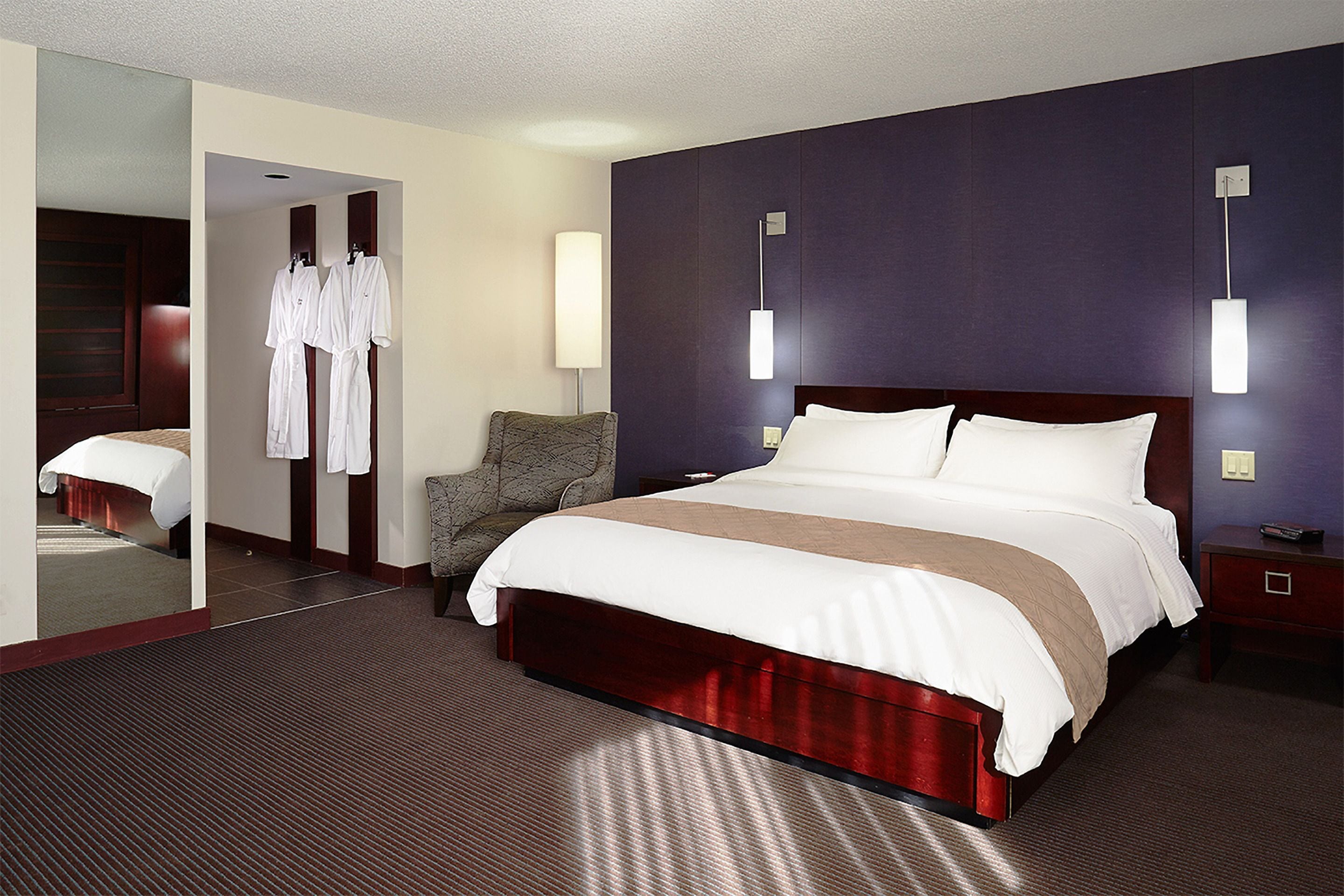 A hotel room with a large bed, a chair, a mirror, and a wardrobe.