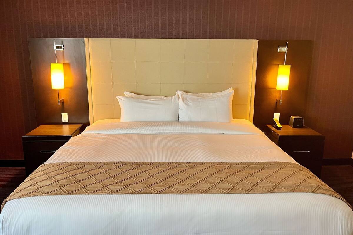 A hotel room with a large bed, two bedside tables, and two wall-mounted lamps.
