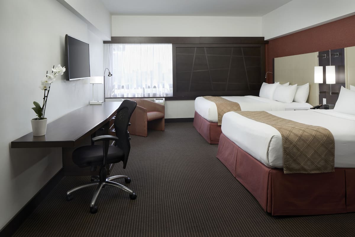 Une chambre d’hôtel avec un lit, un bureau et une chaise, une télévision et une fenêtre avec des rideaux.