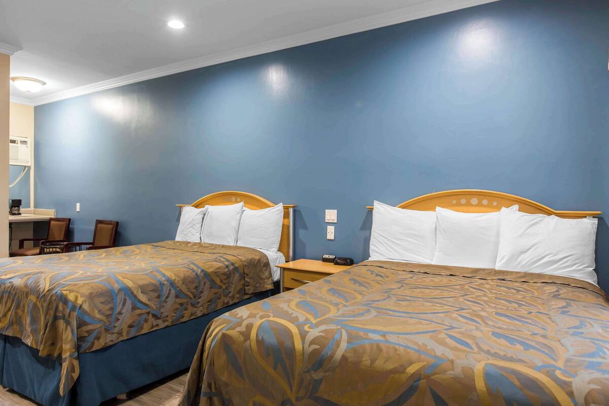 Una camera d'albergo con due letti, una scrivania e una sedia.