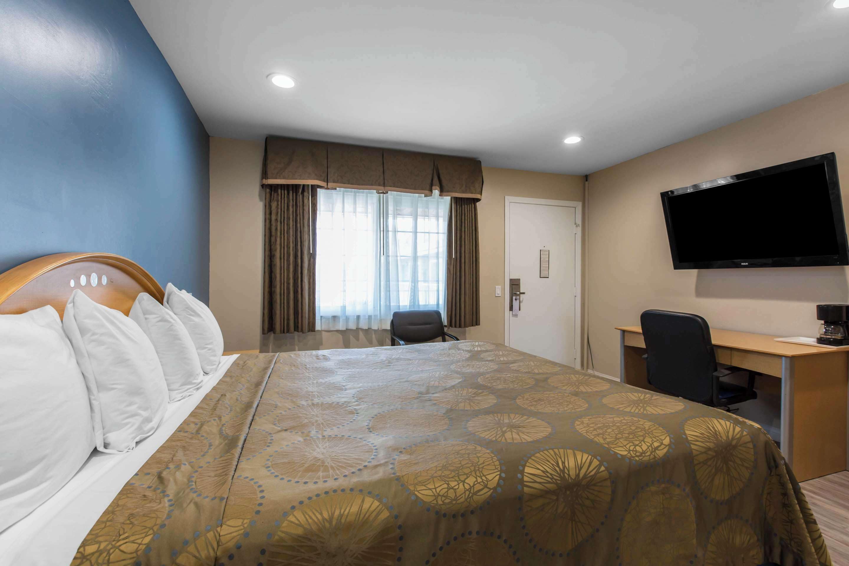 A hotel room with a large bed, a desk, a chair, a television, and a window with curtains.