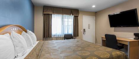 A hotel room with a large bed, a desk, a chair, a television, and a window with curtains.