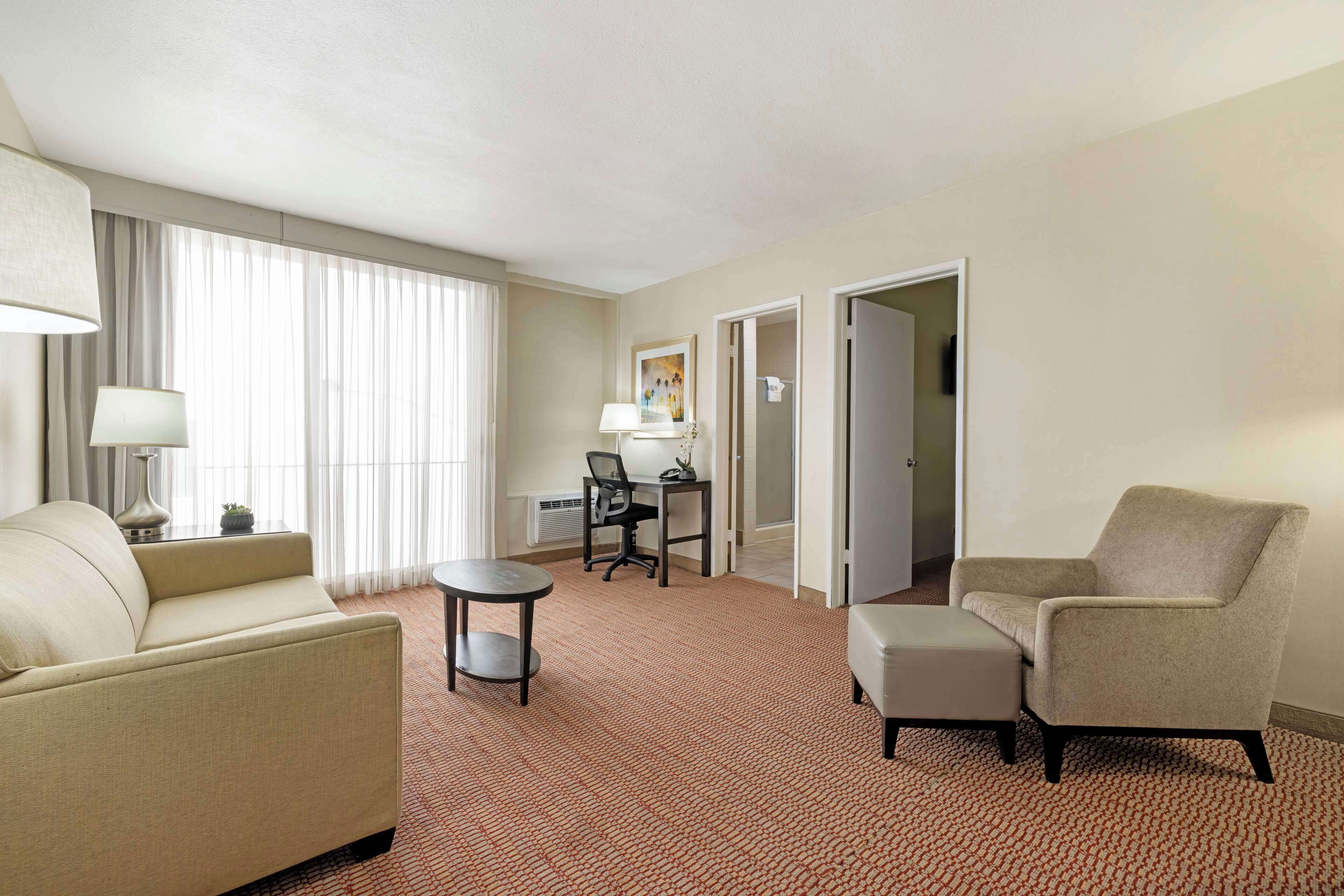 Habitación de hotel con sofá, sillón, una mesita redonda y un escritorio con silla.