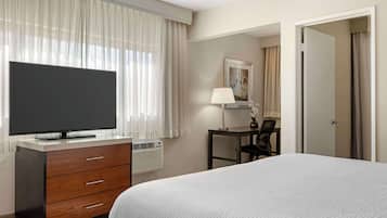 A hotel room with a bed, a TV on a dresser, a desk with a chair, and a door.