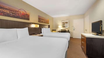 A hotel room with two beds, a television, a desk with a lamp, and artwork on the walls.