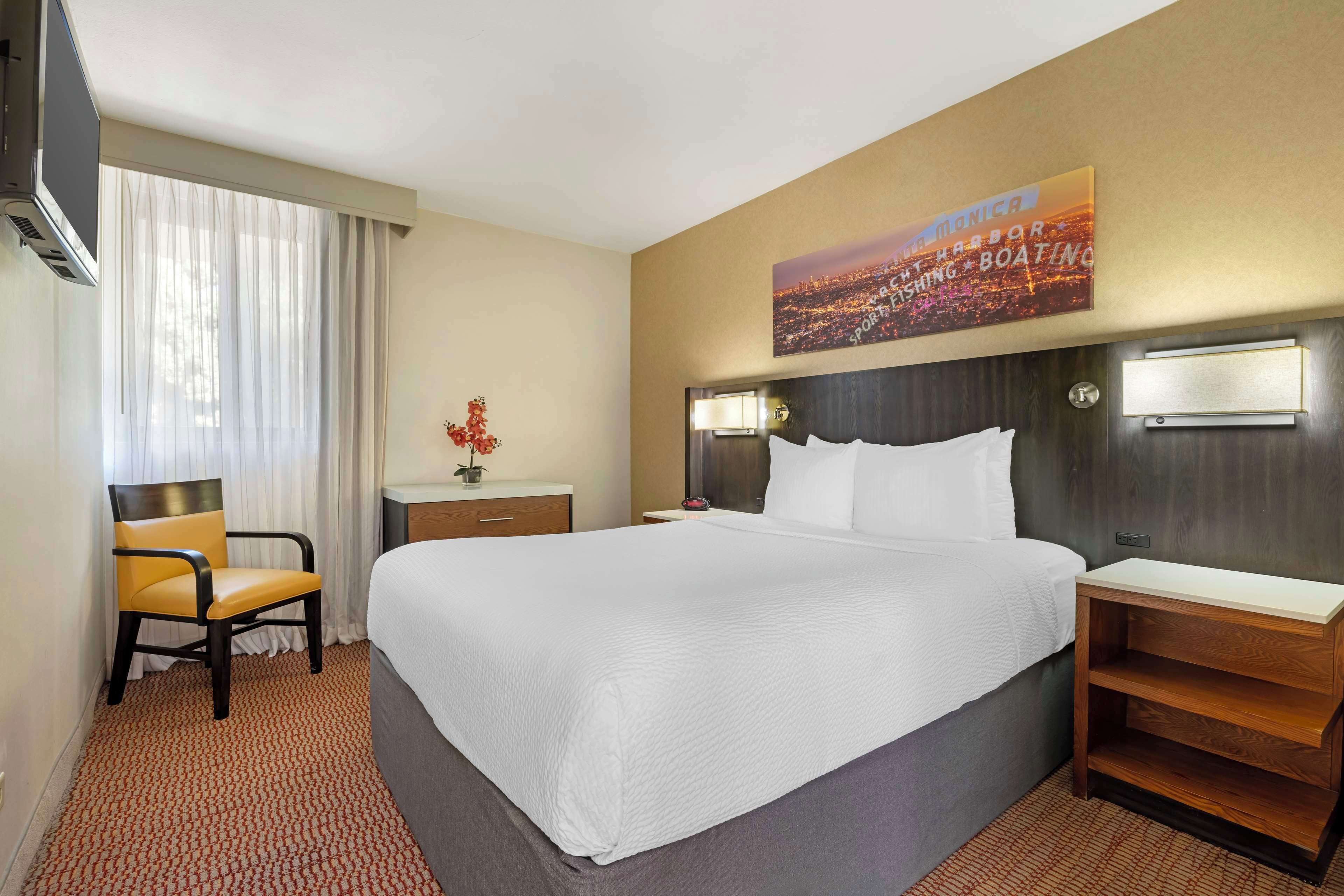 A hotel room with a large bed, a chair, a desk, and a nightstand.