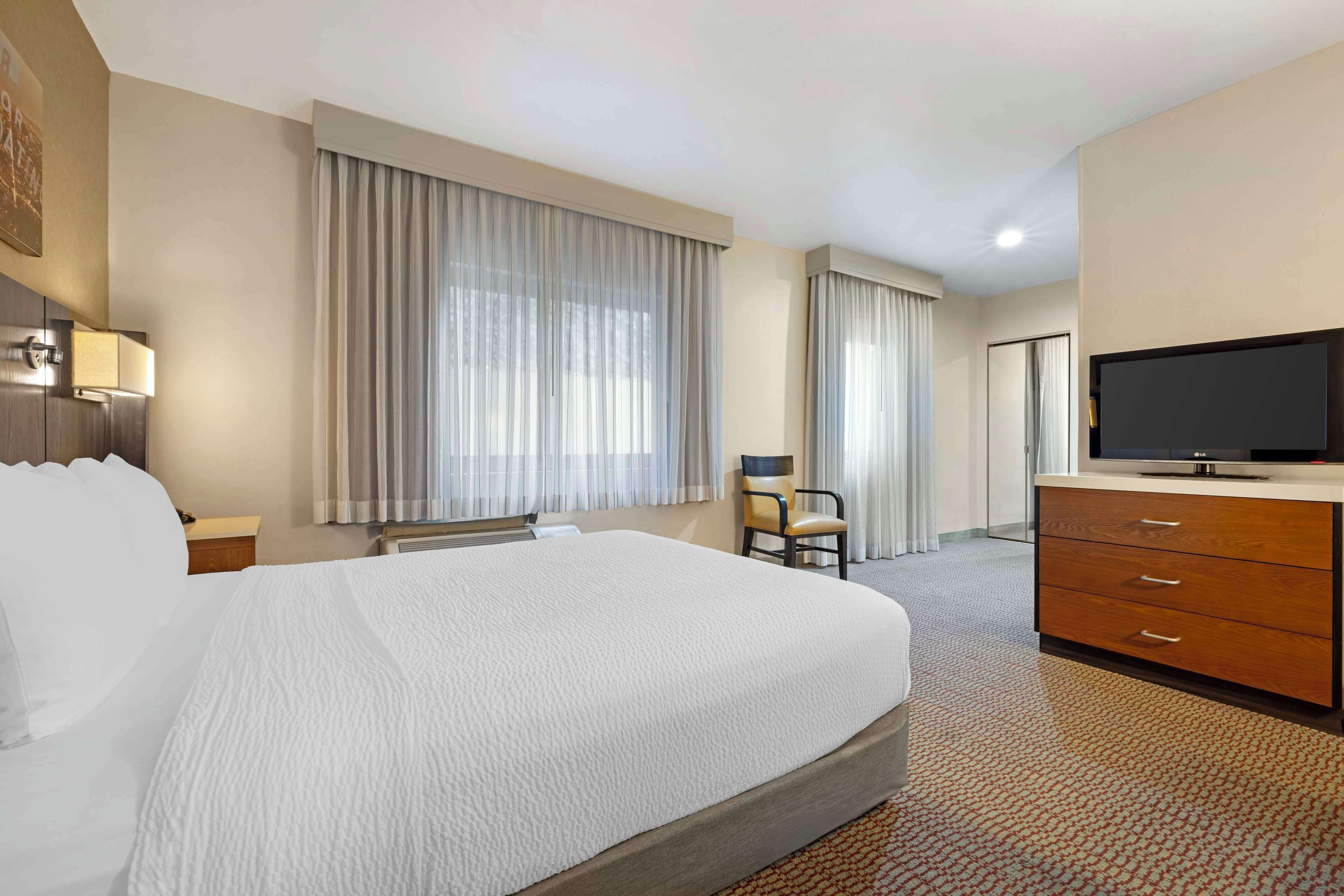 A hotel room with a large bed, a desk with a chair, a television, and a dresser.