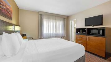 A hotel room with a large bed, a television, a microwave, and a desk with a chair.