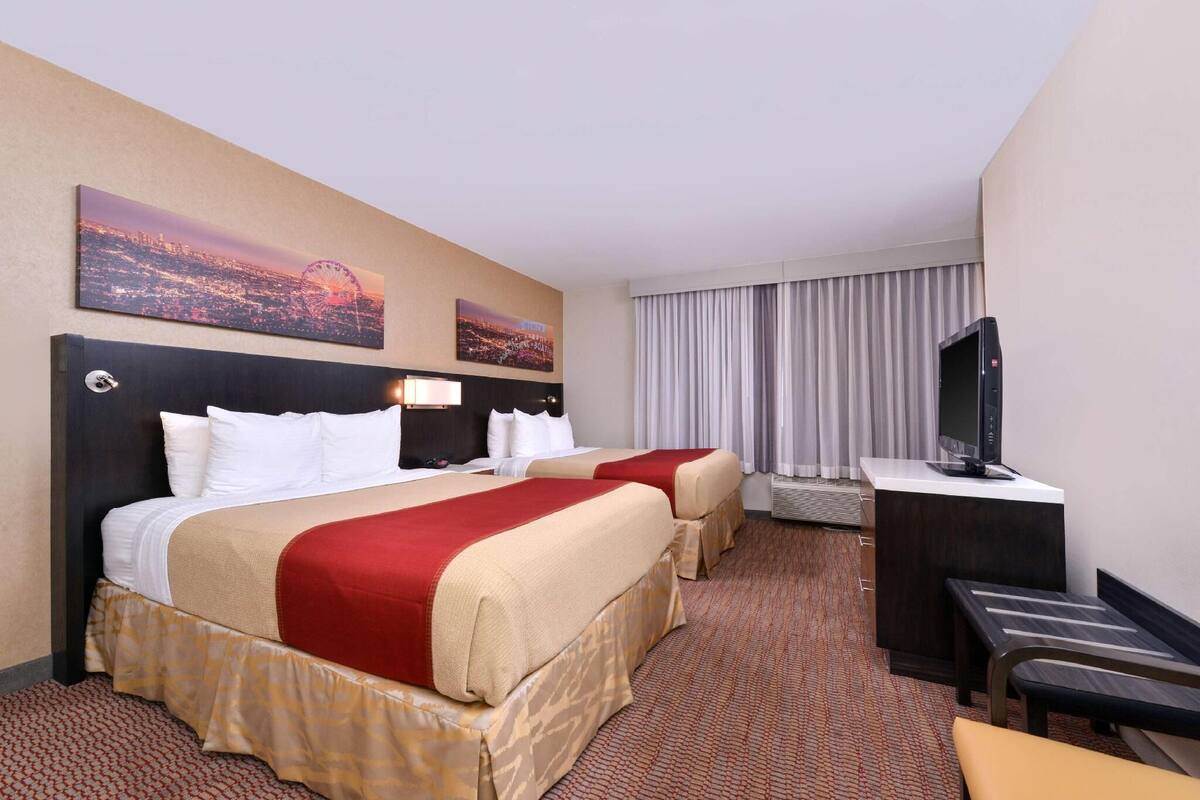 A hotel room with two beds, a desk, a TV, and a window with curtains.