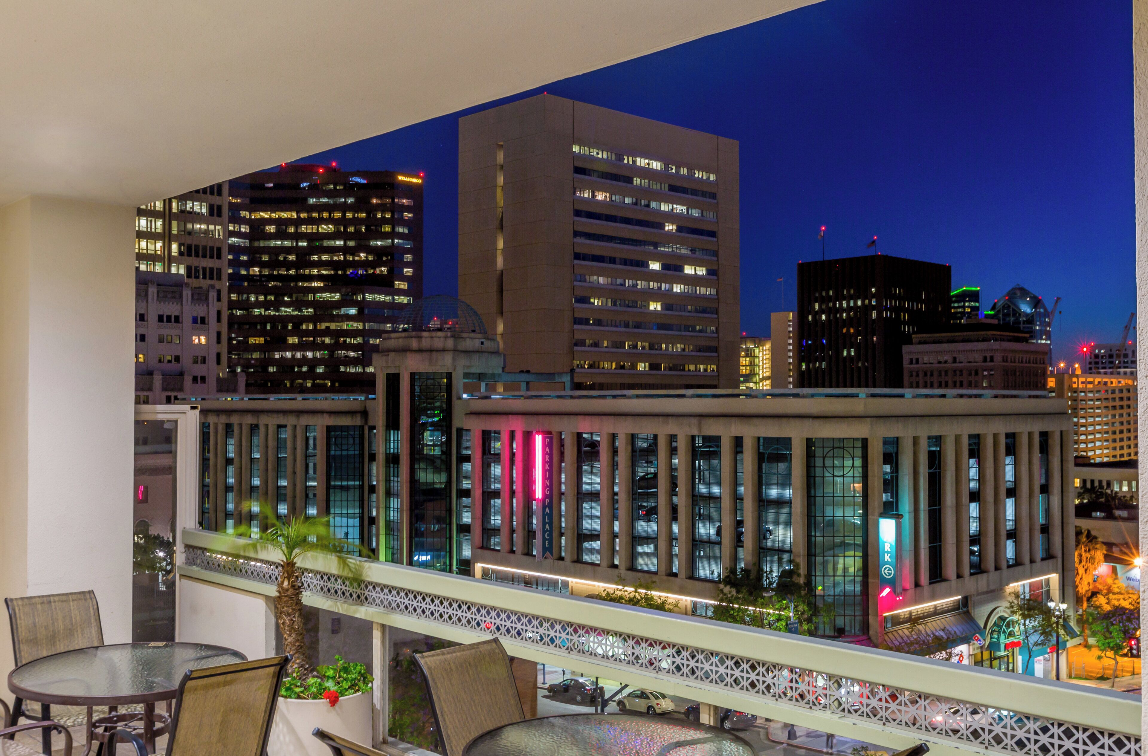 A modern building with a glass facade, a rooftop terrace with outdoor seating, and a view of the city skyline at dusk.