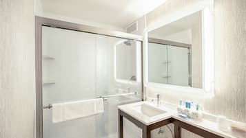 A modern bathroom with a glass shower enclosure, a sink with toiletries, and a large mirror.