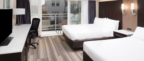 A hotel room with two beds, a desk, a chair, a TV, and a balcony with a view of the city.