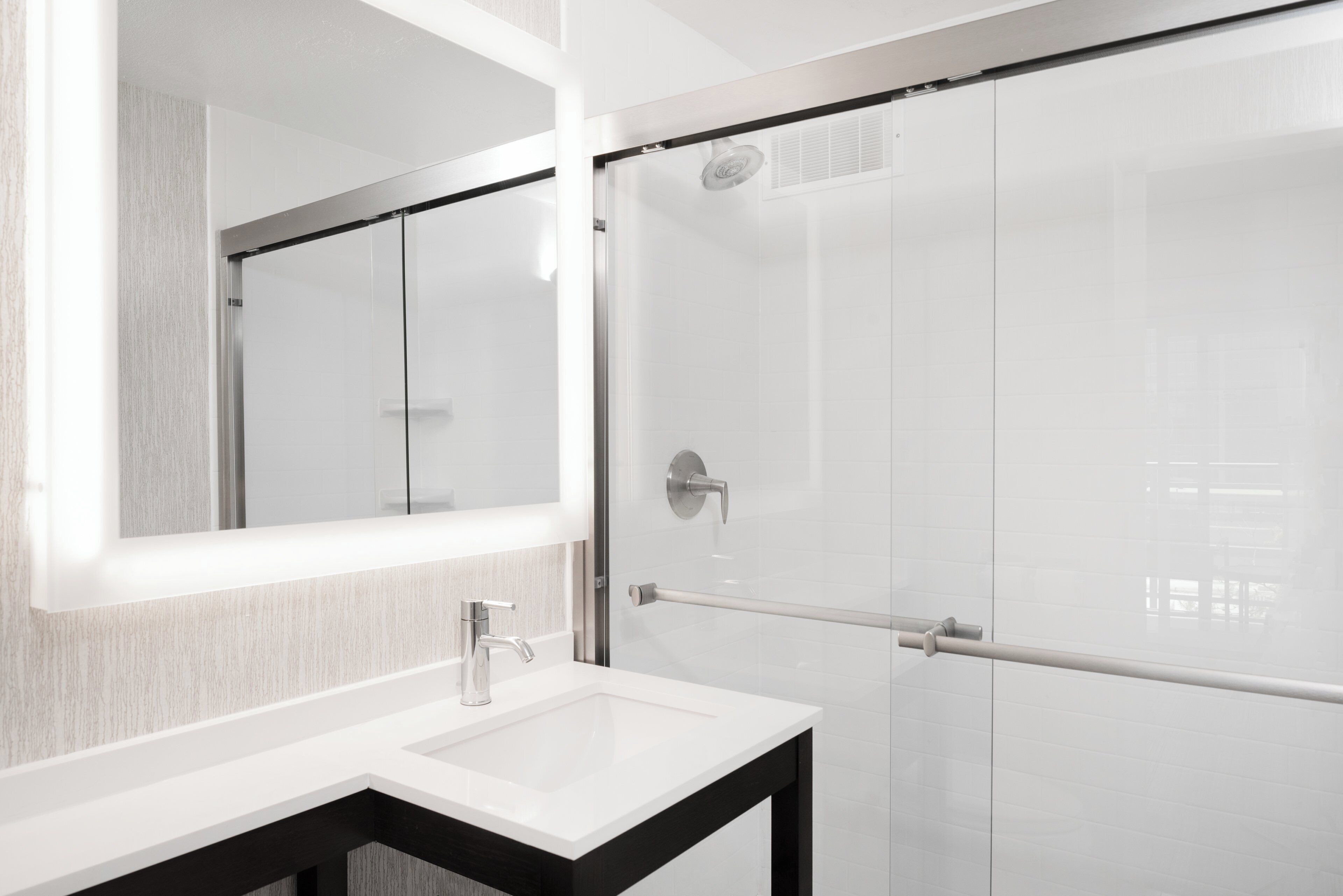 A modern bathroom with a white sink, a large mirror, and a glass shower enclosure.