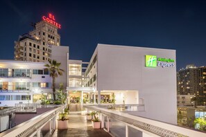 A hotel with a Holiday Inn Express sign, a modern building with balconies, and a view of the city skyline at night. - Holiday Inn Express San Diego Downtown by IHG (San Diego)
