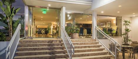 A hotel entrance with a staircase leading to the lobby, glass doors, and indoor plants.