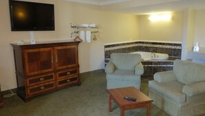 A living room with a TV, a wooden cabinet, a sofa, a small table, and a bathroom with a bathtub and tiled walls. - American Inn (Stockton)