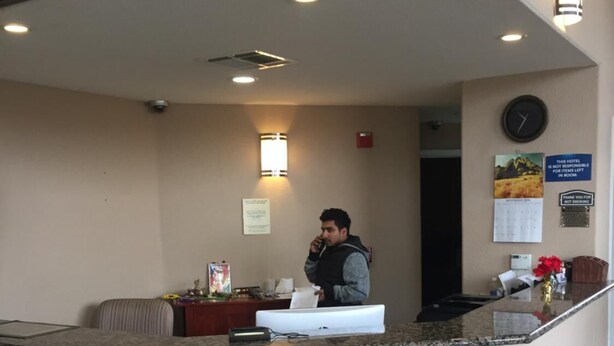 A hotel reception area with a counter, a clock, and a calendar on the wall. - American Inn (Stockton)