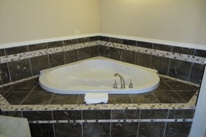 A corner bathroom with a freestanding bathtub, dark patterned tiles, and a white towel on the floor. - American Inn (Stockton)