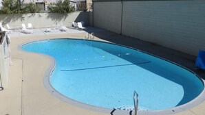 A swimming pool with a curved edge, surrounded by a beige deck and white lounge chairs. - American Inn (Stockton)