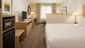 A hotel room with a bed, a desk with a computer, a television, a minibar, and a window with curtains.