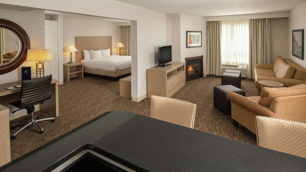 A hotel room with a bed, a TV, a fireplace, a desk with a chair, and a sofa. - DoubleTree by Hilton Portland - Tigard (Tigard)