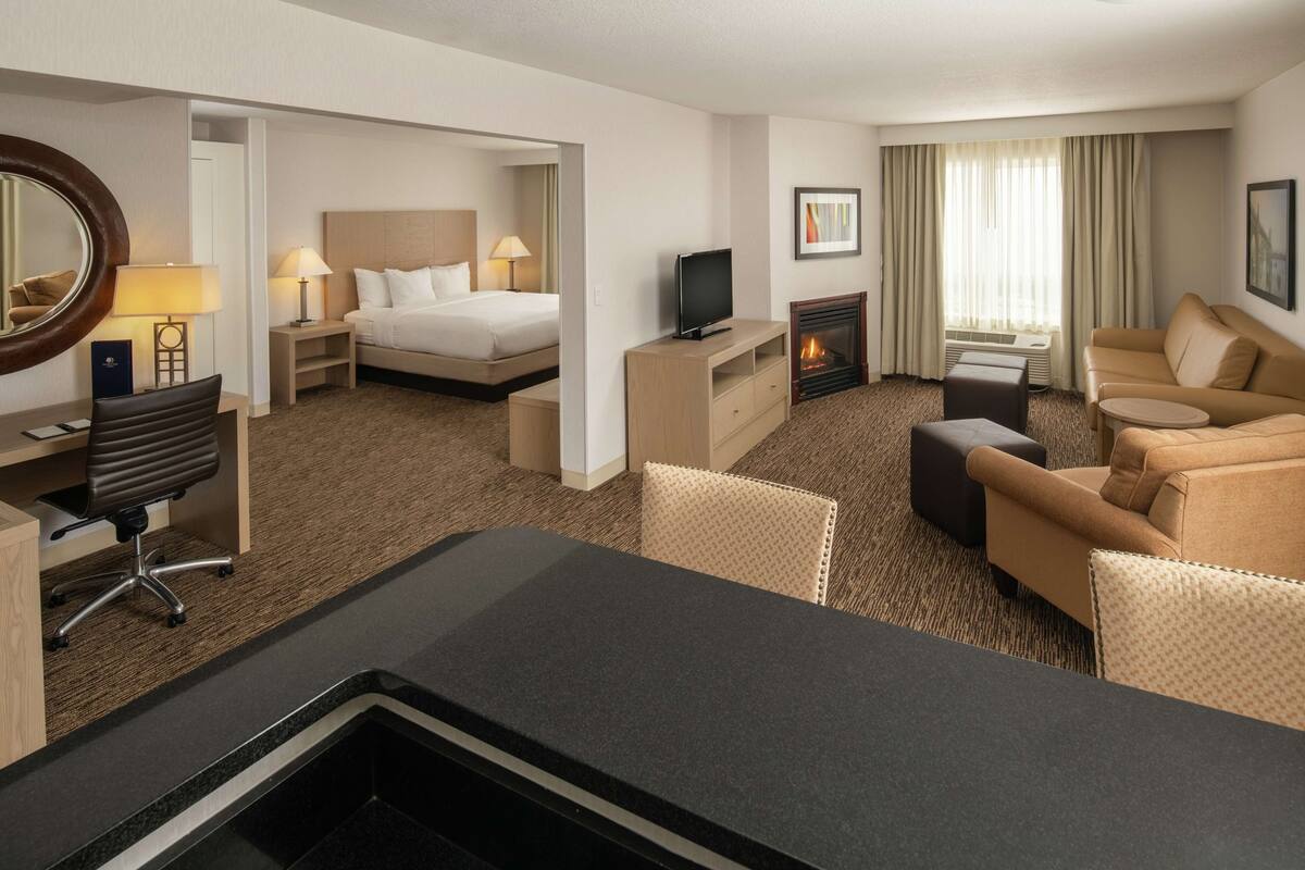 A hotel room with a bed, a TV, a fireplace, a desk with a chair, and a sofa.