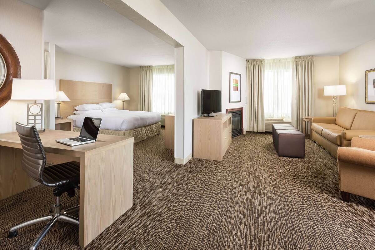 A hotel room with a bed, desk, chair, TV, and a sofa.