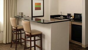 A compact kitchen with a bar area, including a sink, microwave, and coffee maker. There are two bar stools and a framed picture on the wall. - DoubleTree by Hilton Portland - Tigard (Tigard)