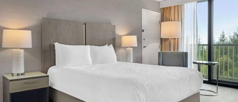 A hotel room with a large bed, two bedside tables with lamps, a chair, and a view of the outdoors.