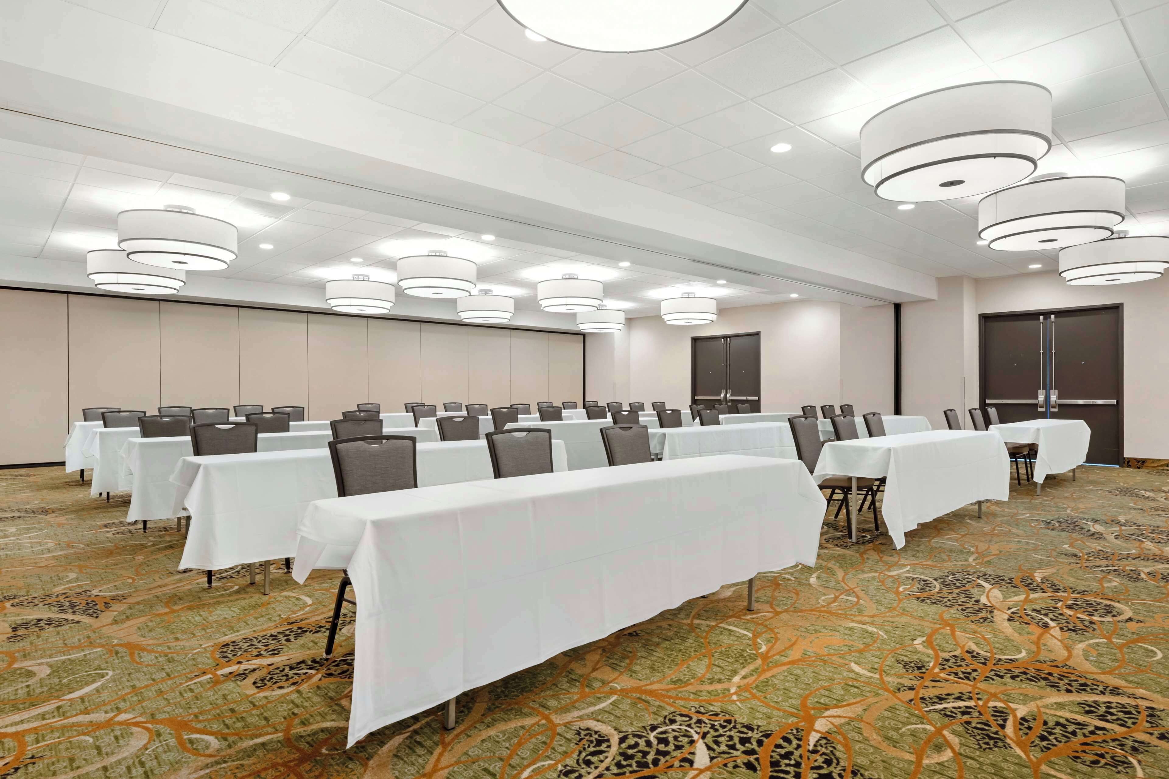 A conference room with multiple tables and chairs, ceiling lights, and a patterned carpet.