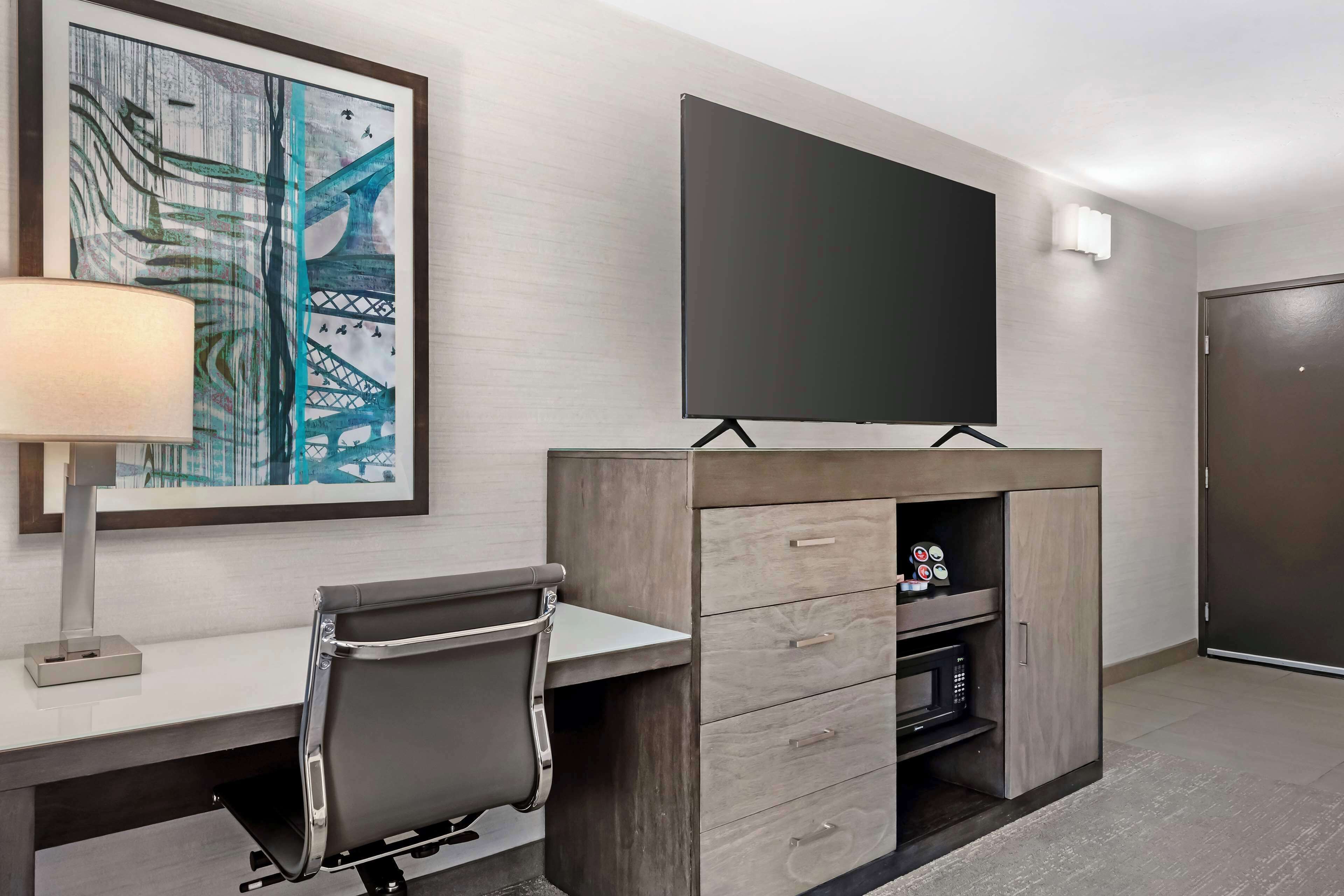 A hotel room with a desk, chair, television, and a framed picture on the wall.