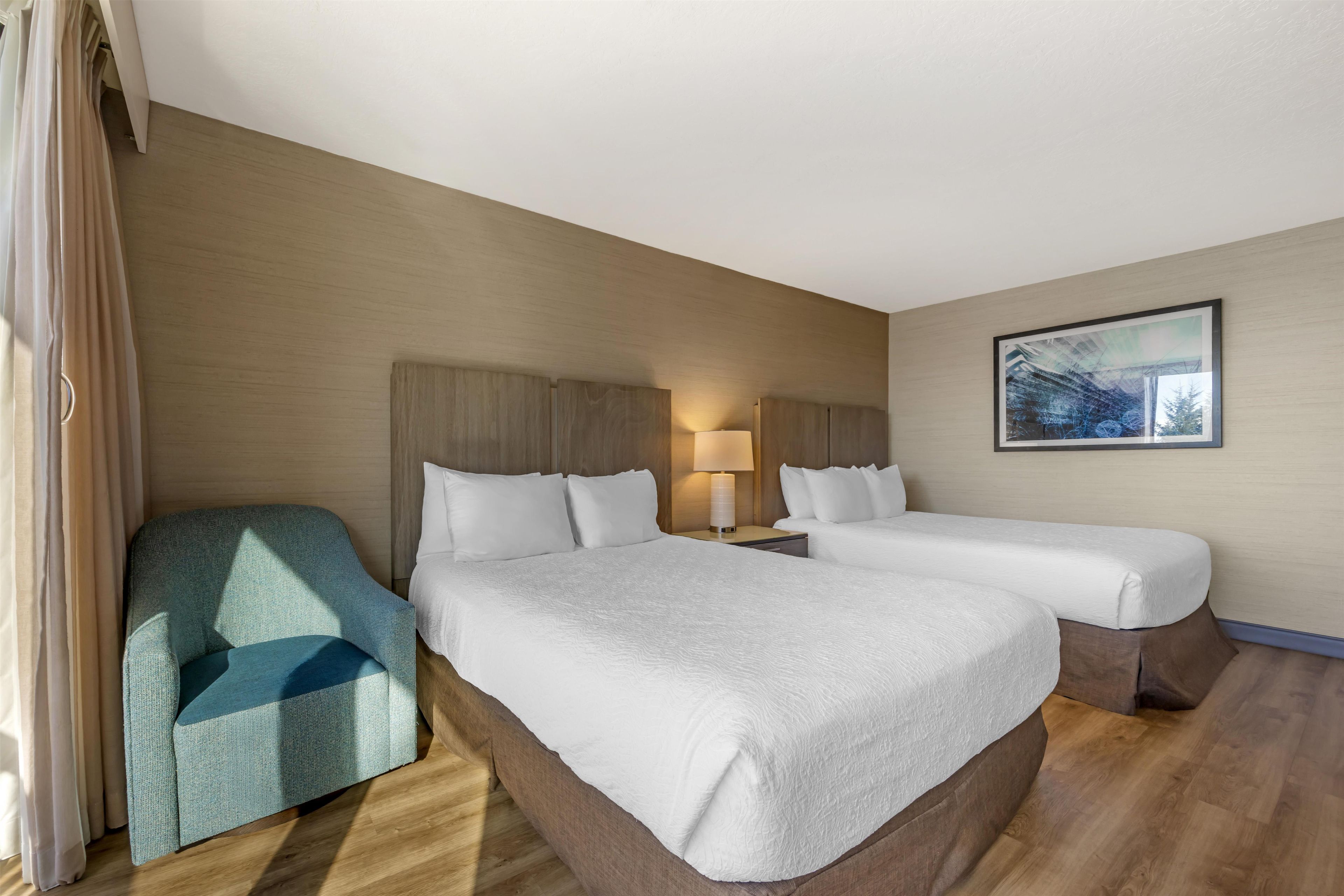 Ein Hotelzimmer mit zwei Betten, einem Sessel, einem Nachttisch, einer Lampe und einem Bild an der Wand.