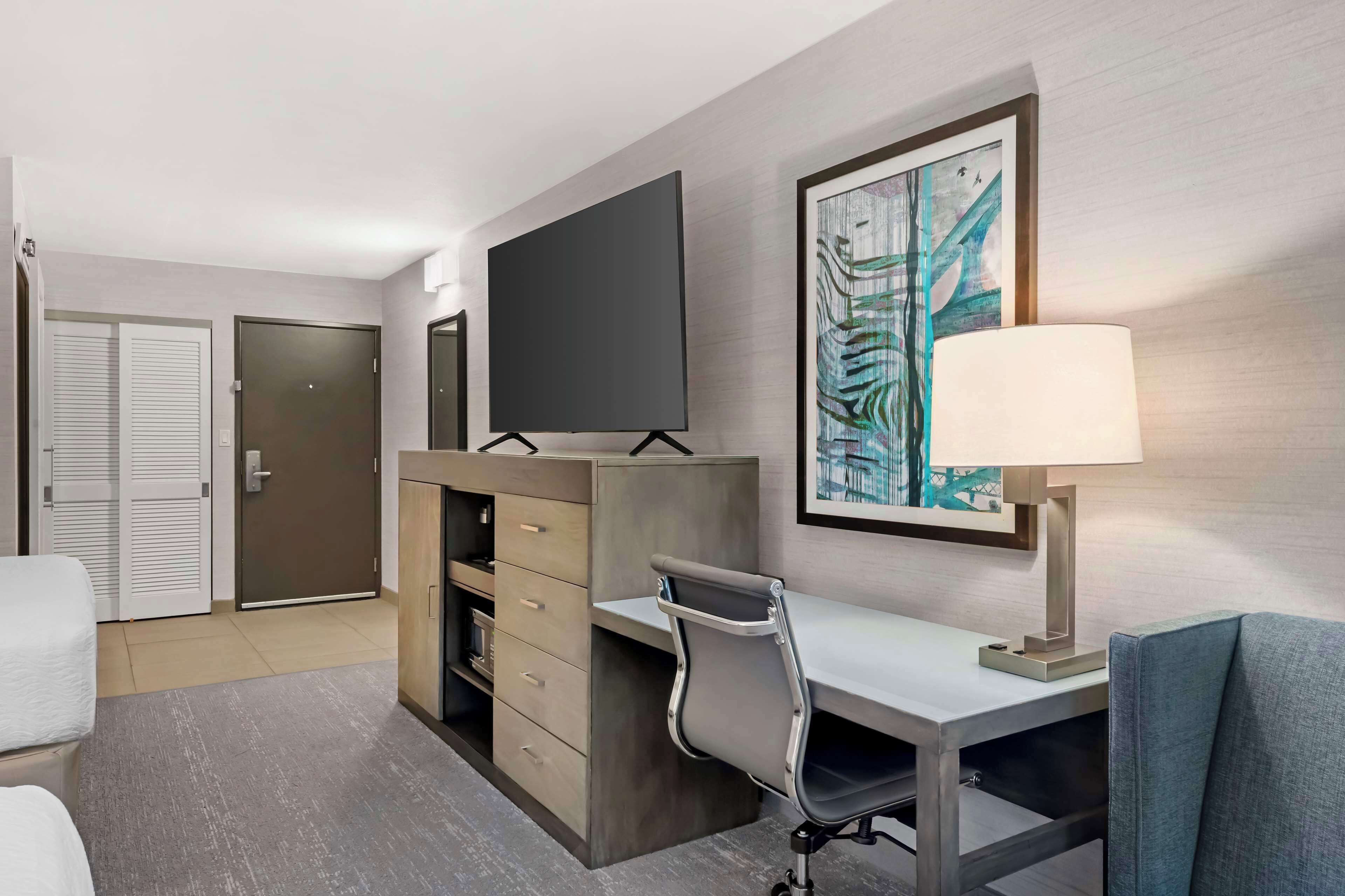 Habitación de hotel con escritorio, silla, televisor y una obra de arte en la pared.