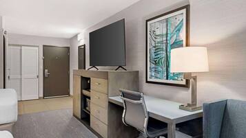 Habitación de hotel con escritorio, silla, televisor y una obra de arte en la pared.