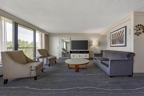 A modern living room with a sofa, armchairs, a coffee table, a TV, and a large window.