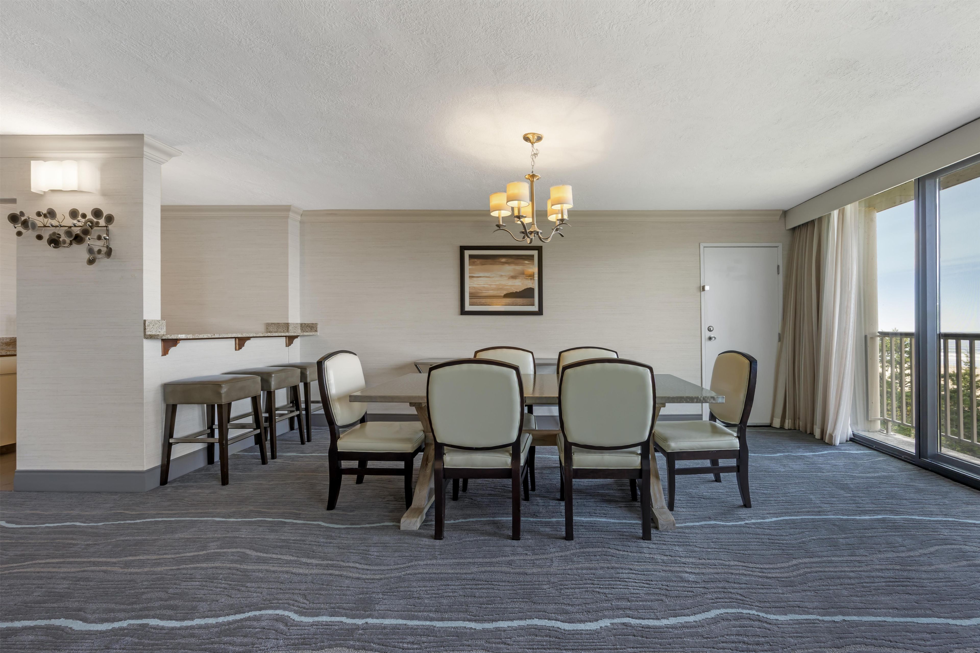 Une salle à manger d’hôtel avec une grande table, des chaises, un lustre et une vue sur l’extérieur.