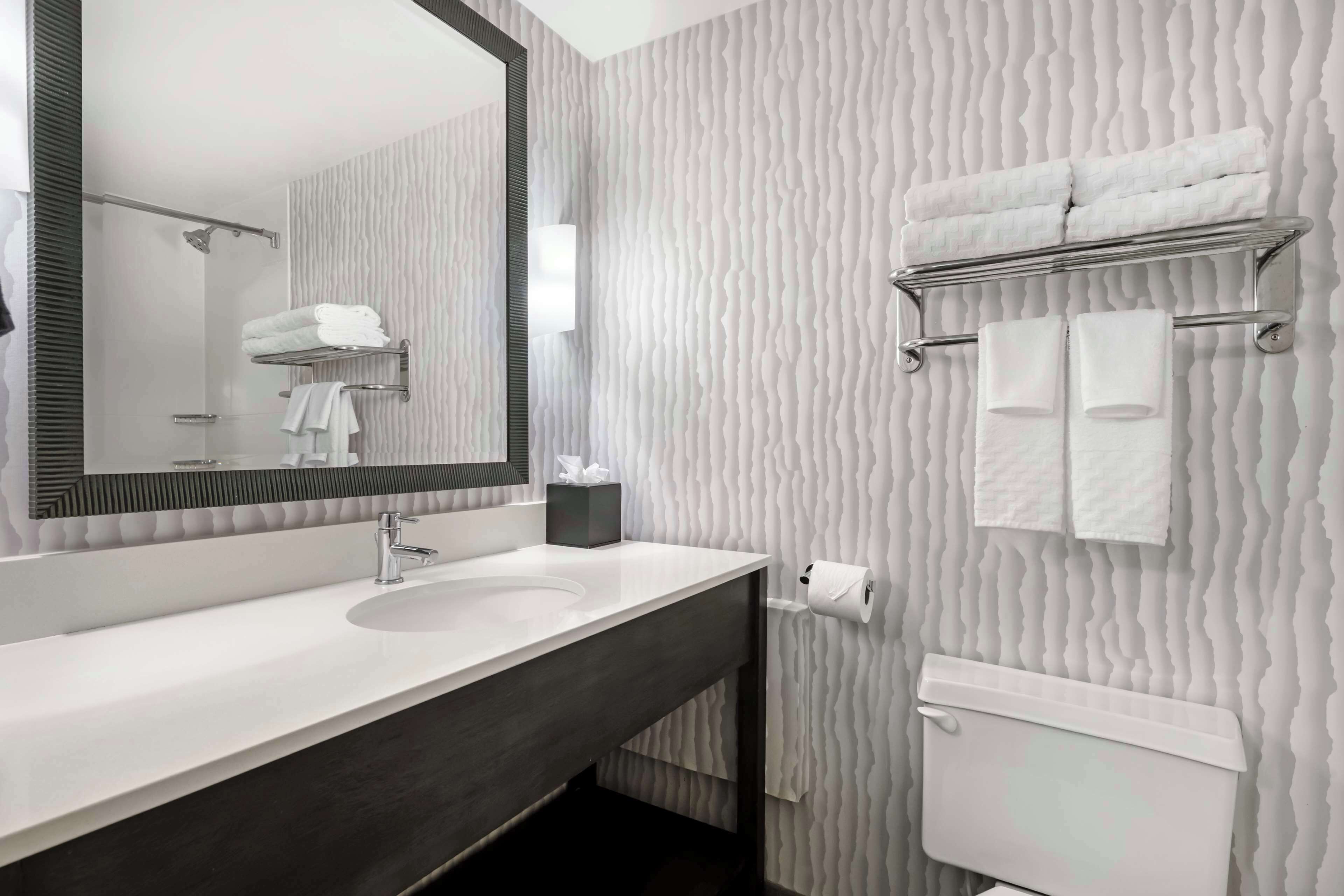 Un baño moderno con un lavamanos blanco, un espejo grande, un perchero para toallas y un inodoro.
