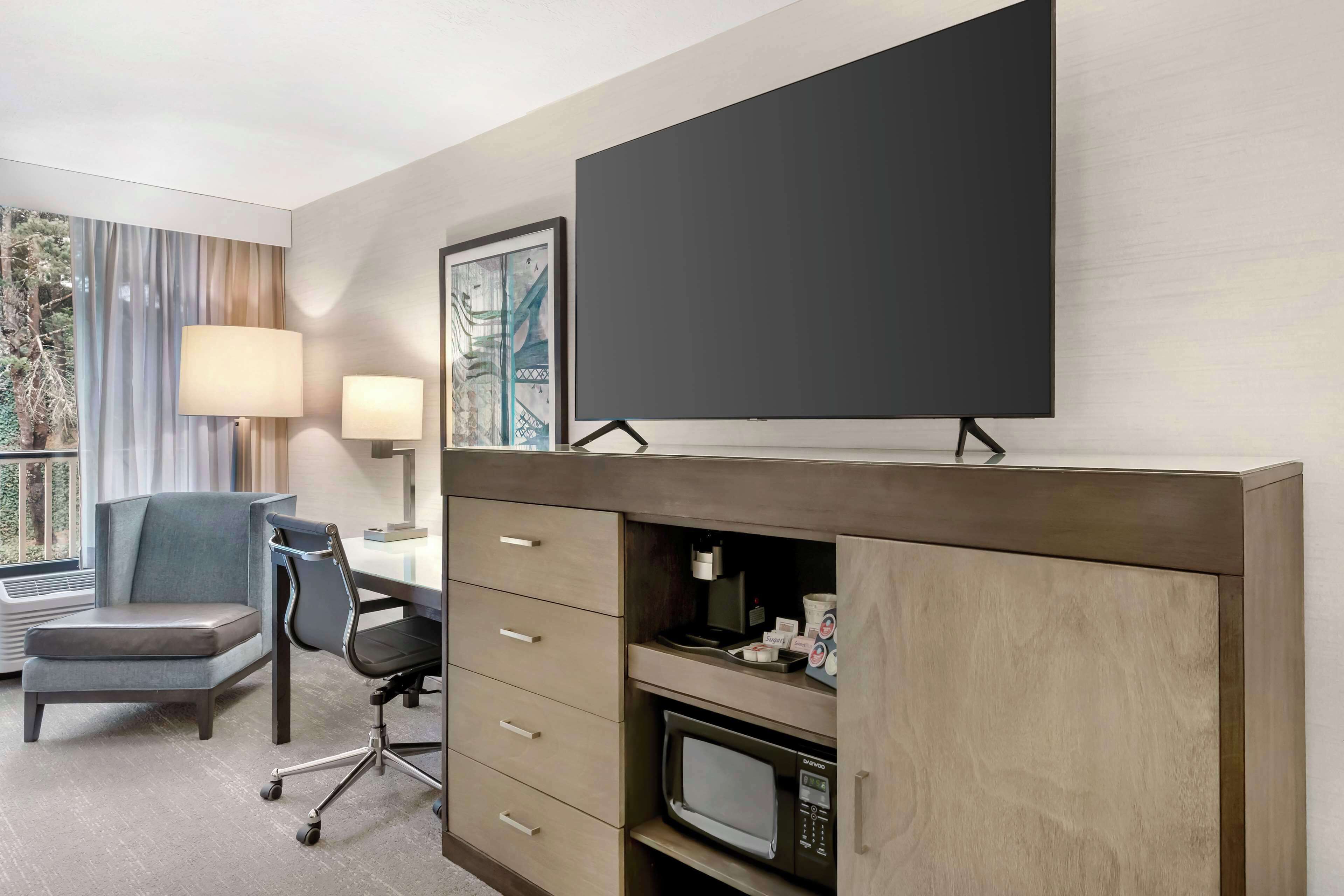 Quarto de hotel com televisão de tela plana, uma escrivaninha com cadeira, máquina de café e micro-ondas.