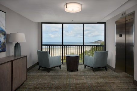 A room with two armchairs, a small table, a lamp, and a view of the sea through large windows.