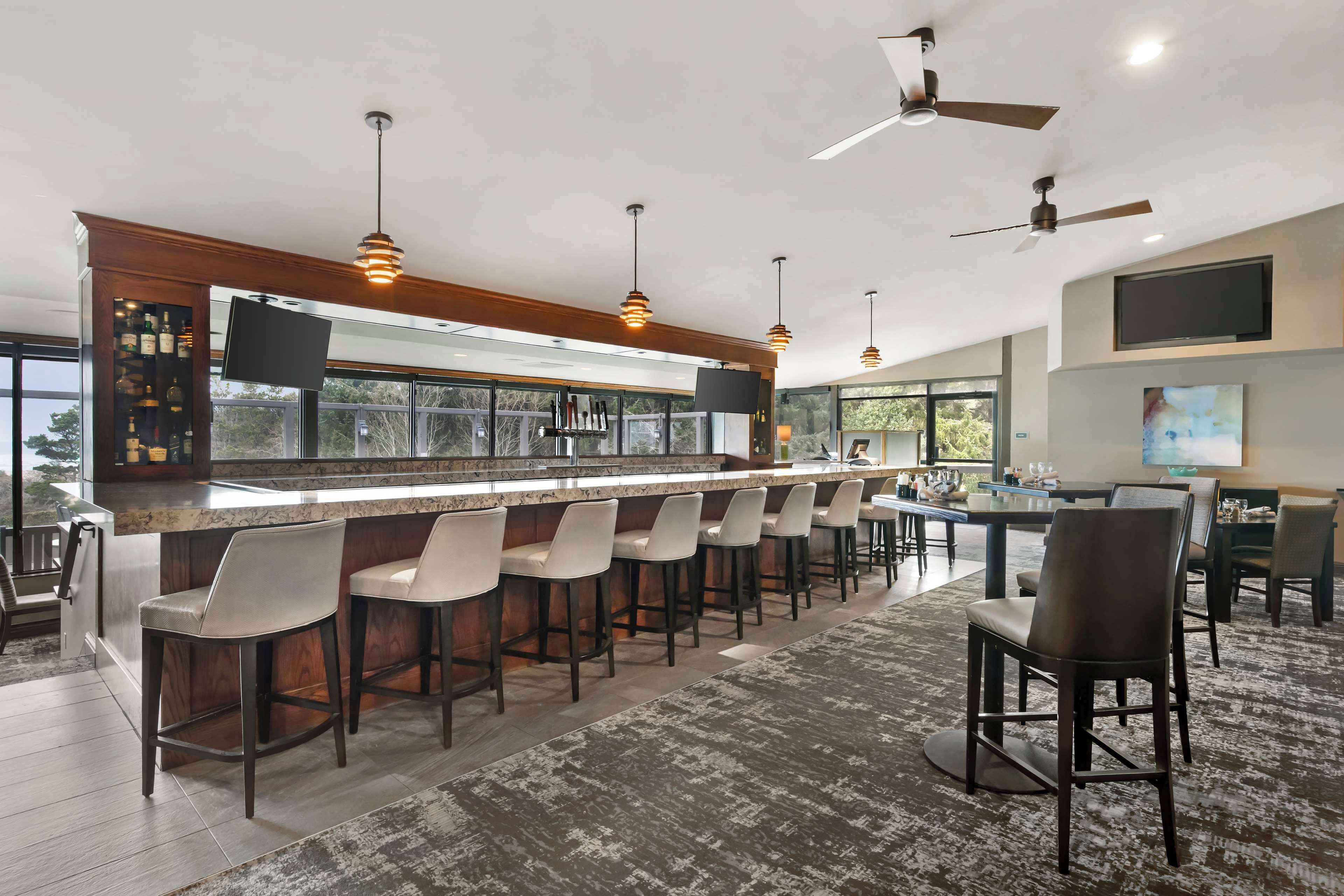 A bar area with a long counter, multiple stools, ceiling fans, and a television mounted on the wall.