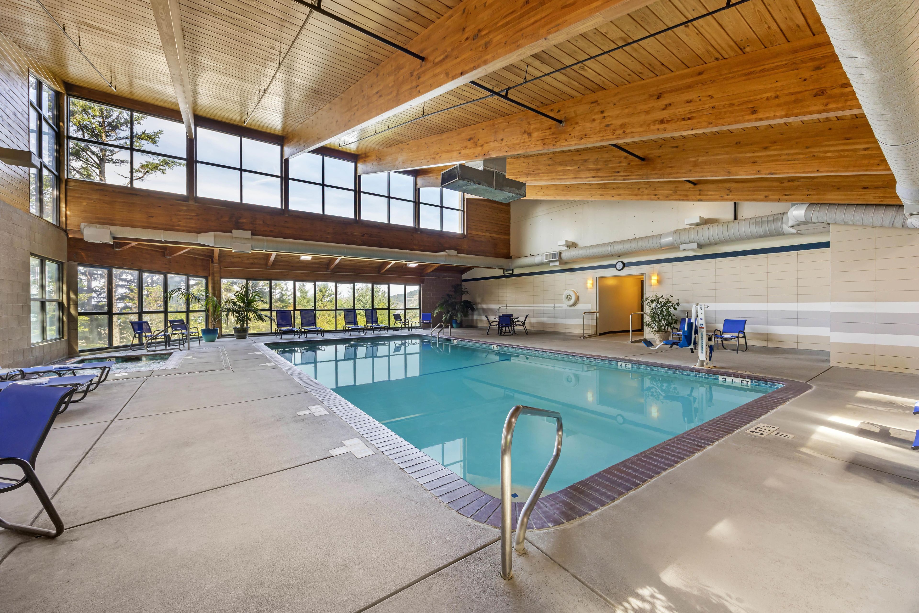 An indoor swimming pool with a wooden ceiling, clear windows, and lounge chairs.