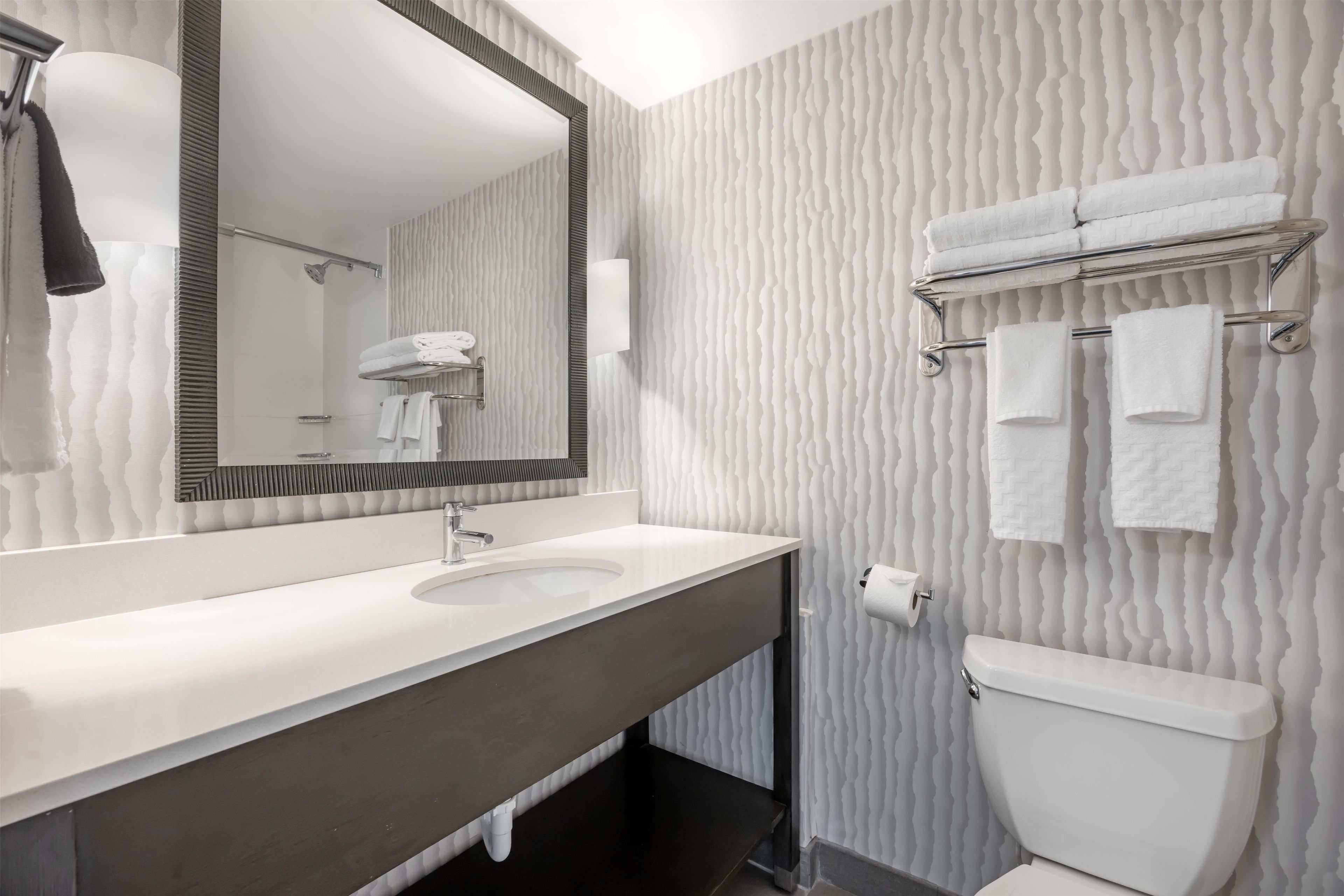 Un baño moderno con un espejo grande, un lavabo, un inodoro y un perchero para toallas.