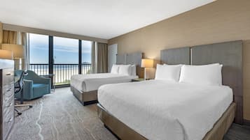 A hotel room with two beds, a desk, a chair, and a view of the ocean.