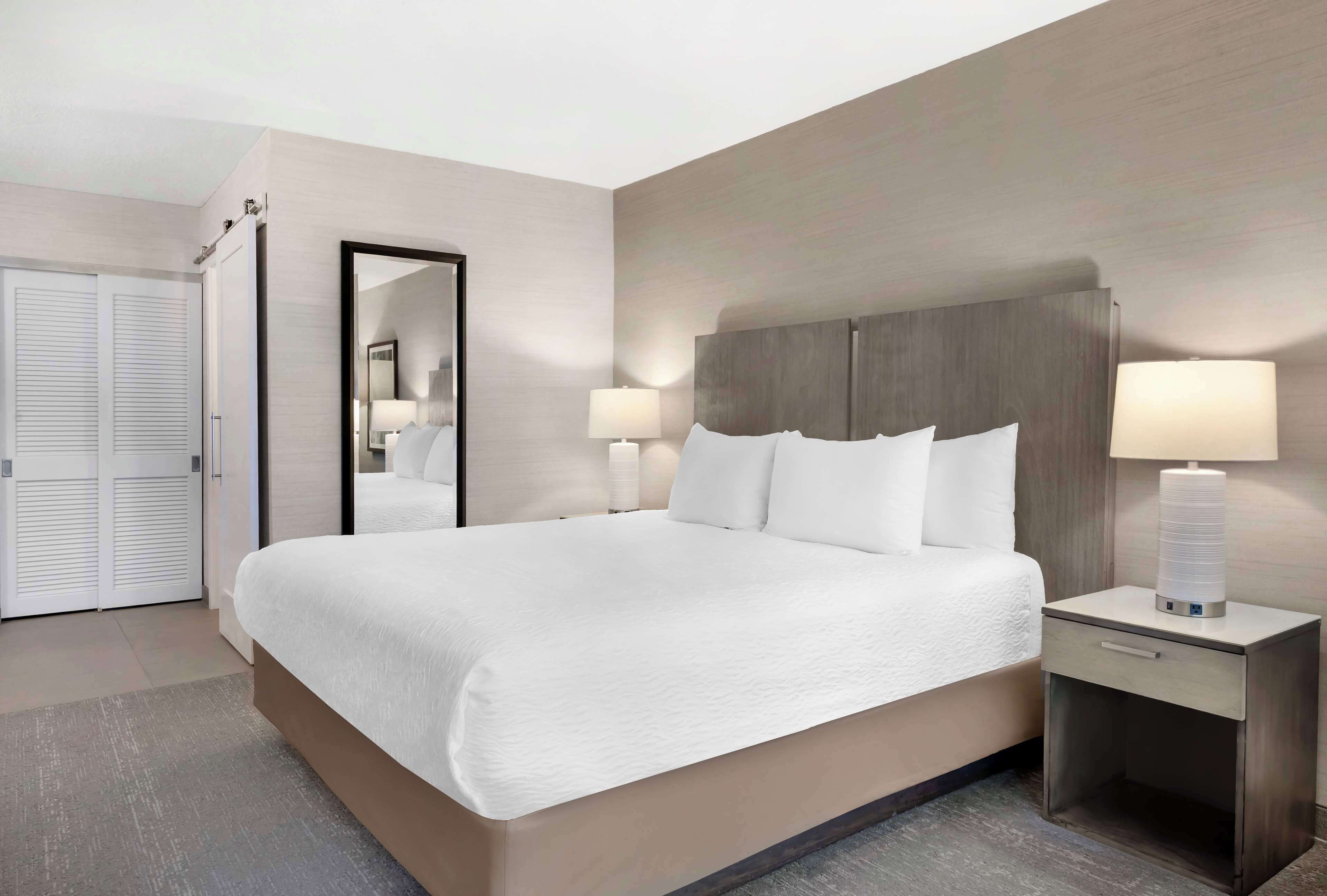 A hotel room with a large bed, bedside tables with lamps, a mirror, and a wardrobe.