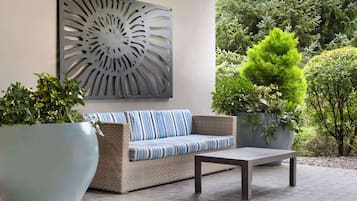A patio area with a sofa, a table, and potted plants.