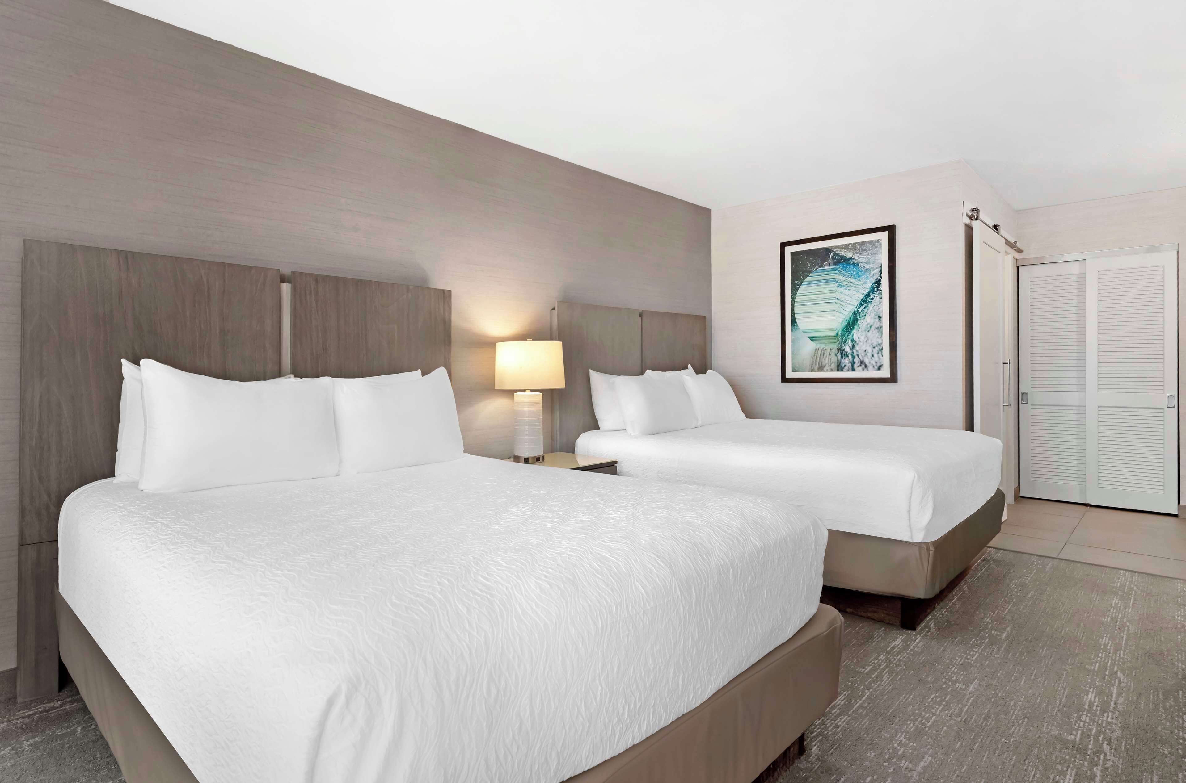 Een hotelkamer met twee bedden, een nachtkastje met een lamp, een lijst met een foto aan de muur en een schuifdeur.