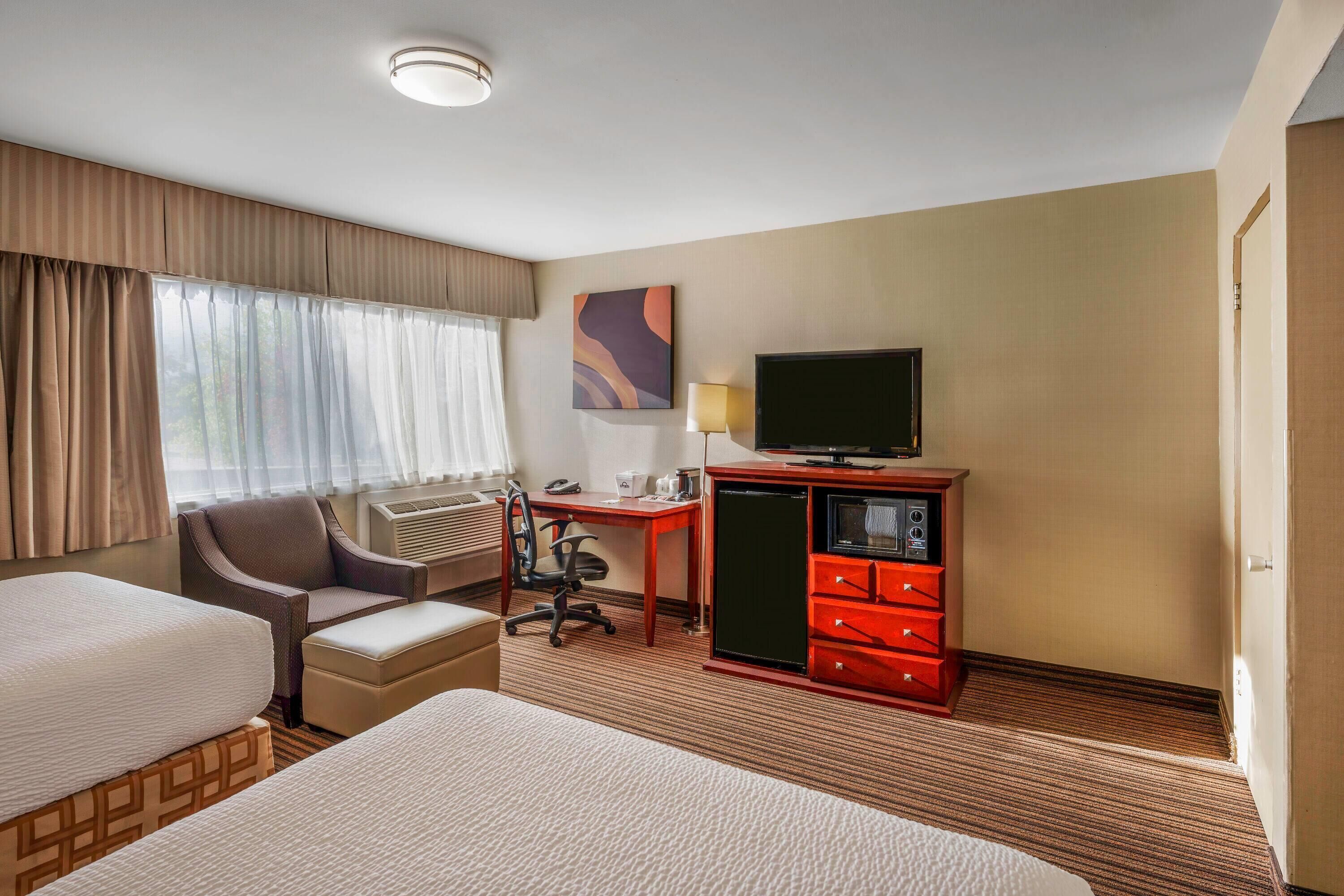 Quarto de hotel com duas camas, uma escrivaninha, uma cadeira, uma TV e um minibar.
